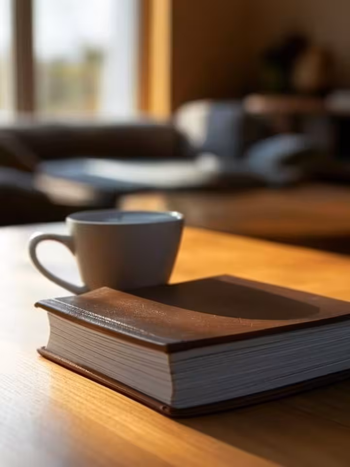 symbolic image of a closed book on a minimalist wooden table with a coffee cup beside it, representi